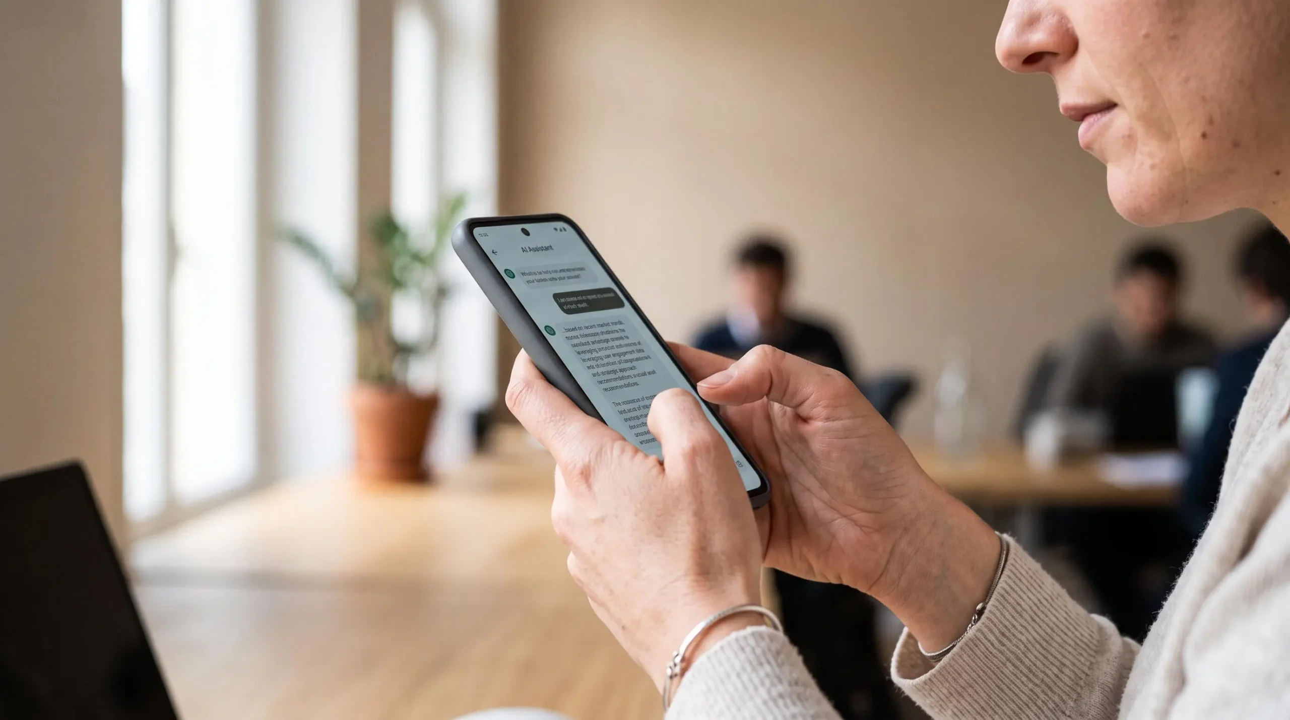 Professionnel utilisant un smartphone pour consulter un assistant IA génératif pour une recherche de travail dans un espace de coworking